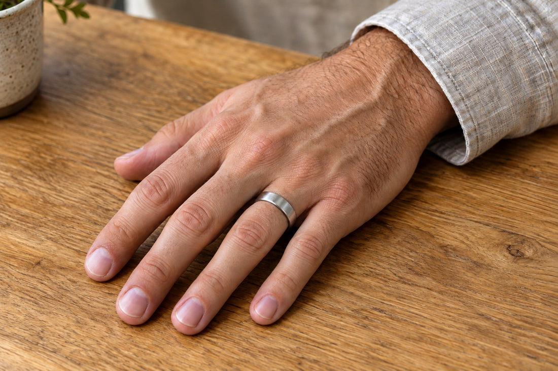 A silver wedding band on the ring finger of a man's left hand