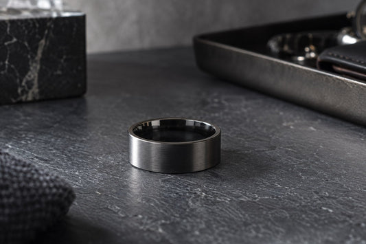 A brushed tungsten wedding band on a dark slate surface